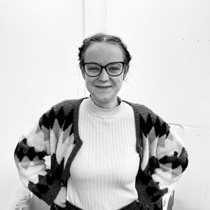 smiling older woman with short blonde hair wearing a coral sweater and green top in a neutral background 15 years of wisdom