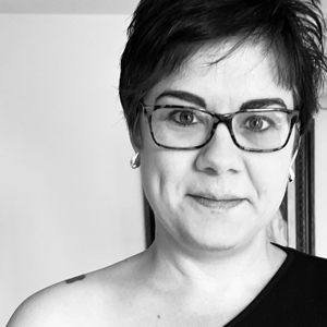 woman with short dark hair wearing glasses and a black top smiling in a black and white photo representing confidence and style 9 qualities