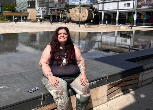 woman sitting by water in a public space wearing floral leggings with a reflective modern sculpture nearby perfect for enjoying sunny days and exploring the number 13