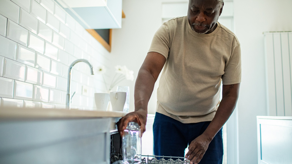 man loading dishwasher with water bottle in modern kitchen doing household chores