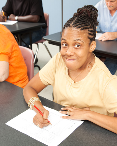 young woman smiling while writing on paper in classroom environment with other students engaged in similar activities learning and collaboration 2 education 2 study