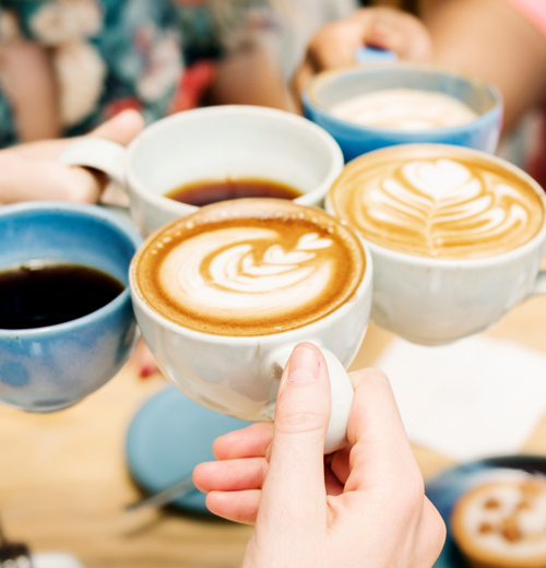 group of hands cheering with coffee cups featuring latte art various coffee types in cozy setting