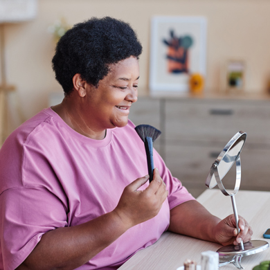 woman looking in a mirror applying makeup with a brush in a bright room featuring beauty products and a decorative wall art capturing beauty routine and makeup tips 3 different styles