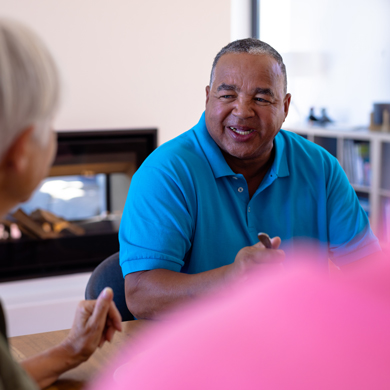 smiling man in blue shirt engaging in conversation with older adults around a table discussing topics together 2 people 2 conversations