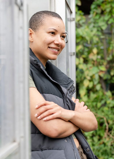 smiling woman wearing a vest standing outdoors with crossed arms in a gardenscape three elements of nature