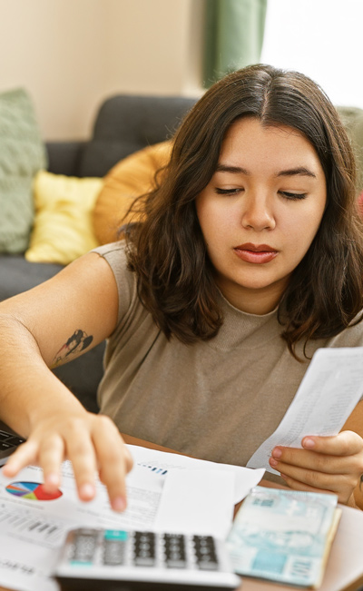 woman analyzing financial documents while using a calculator and organizing papers in a home office setting focusing on budgeting and expenses