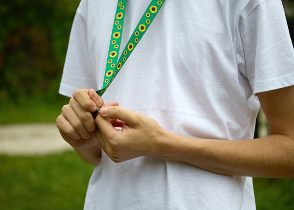 person wearing a white t-shirt adjusting a colorful lanyard outdoors four styles of lanyards