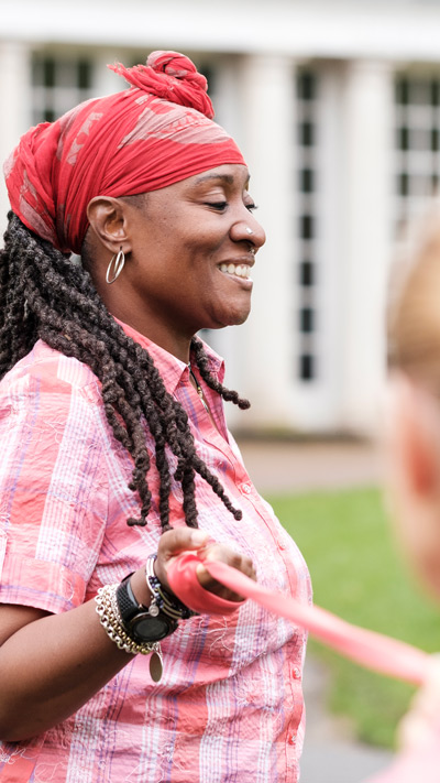 smiling woman with long braids wearing a red headwrap and pink shirt holding a leash outside capturing joyful moments in nature