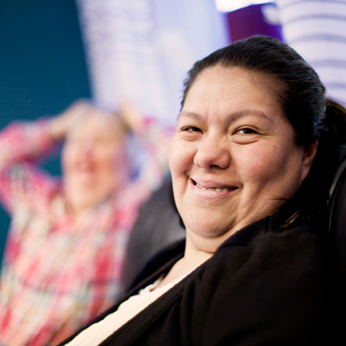 smiling woman sitting in a chair with a blurred background of another person enjoying a moment of happiness three smiling faces