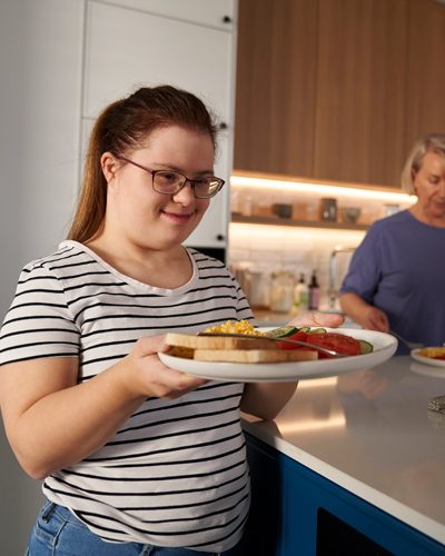 young woman holding a plate of breakfast featuring eggs toast and tomatoes with a joyful expression in a modern kitchen setting cooking and family meals