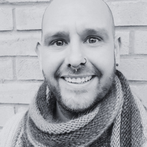 smiling person with shaved head wearing a scarf against a brick wall highlighting 8 different styles